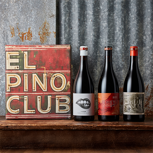Three bottles of El Pino Club wines on a table with an El Pino Club sign and a metal backdrop
